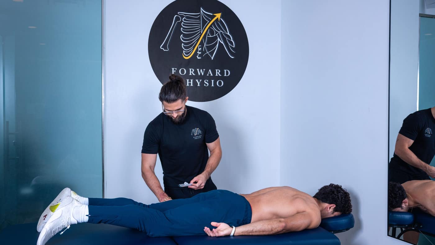 Forward Physio doctor of physical therapy beside an athlete lying face-down on a treatment table — the position used for calf strain assessment and hands-on treatment in Tampa.