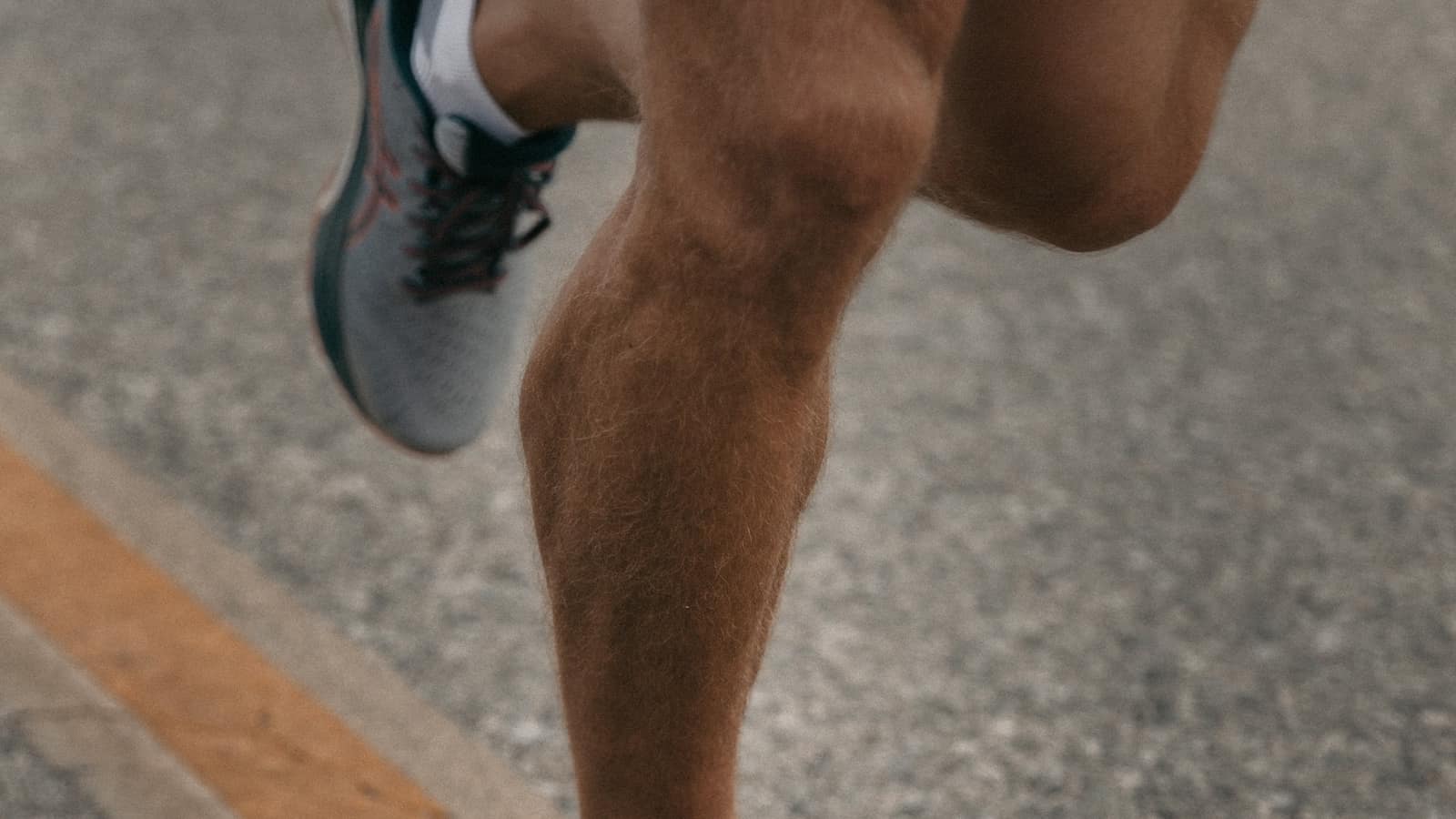 Close-up of a runner’s calf muscle working mid-stride on an asphalt road — the push-off that calf strain physical therapy in Tampa gets runners back to.