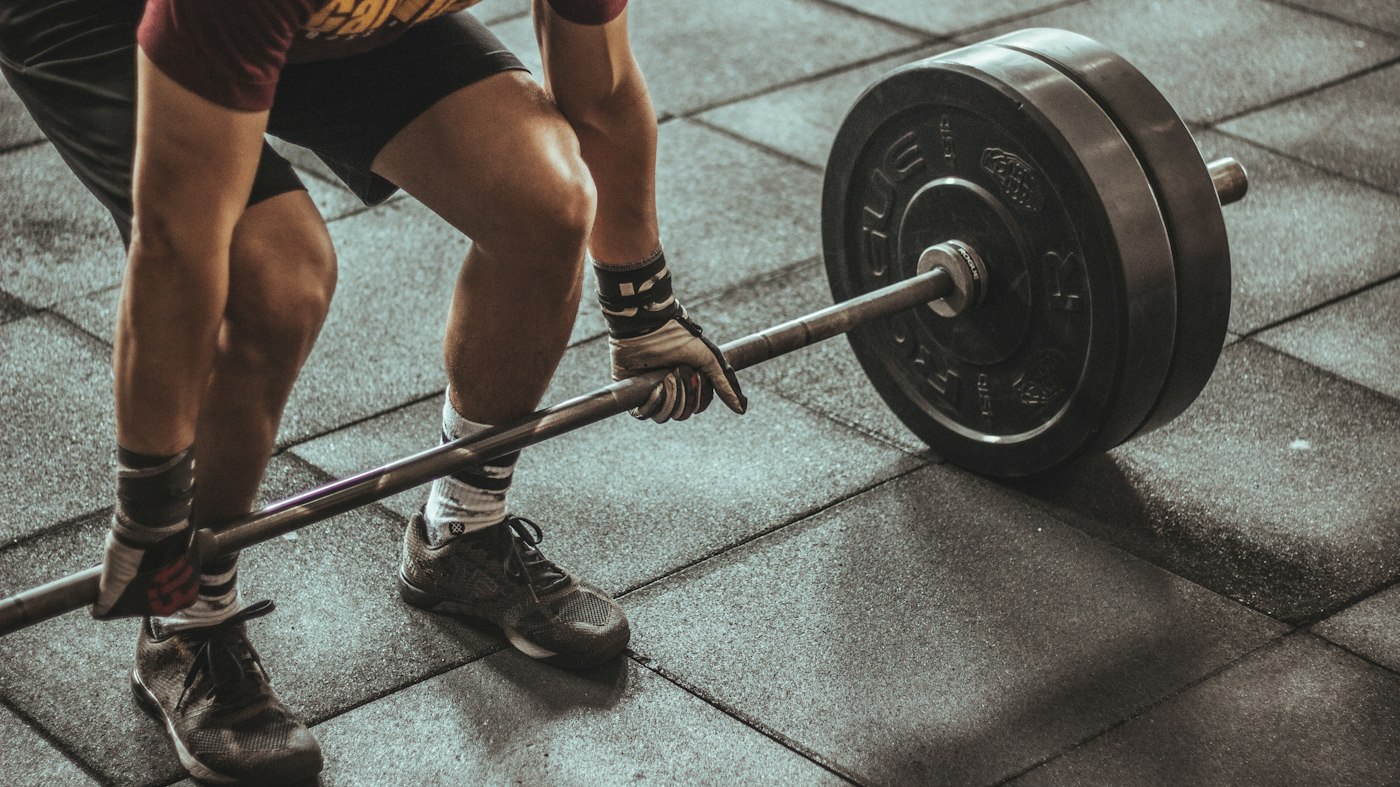 Athlete set up over a loaded barbell on a gym floor — the progressive hip-hinge loading that rebuilds hamstring strength during hamstring strain rehab in Tampa.