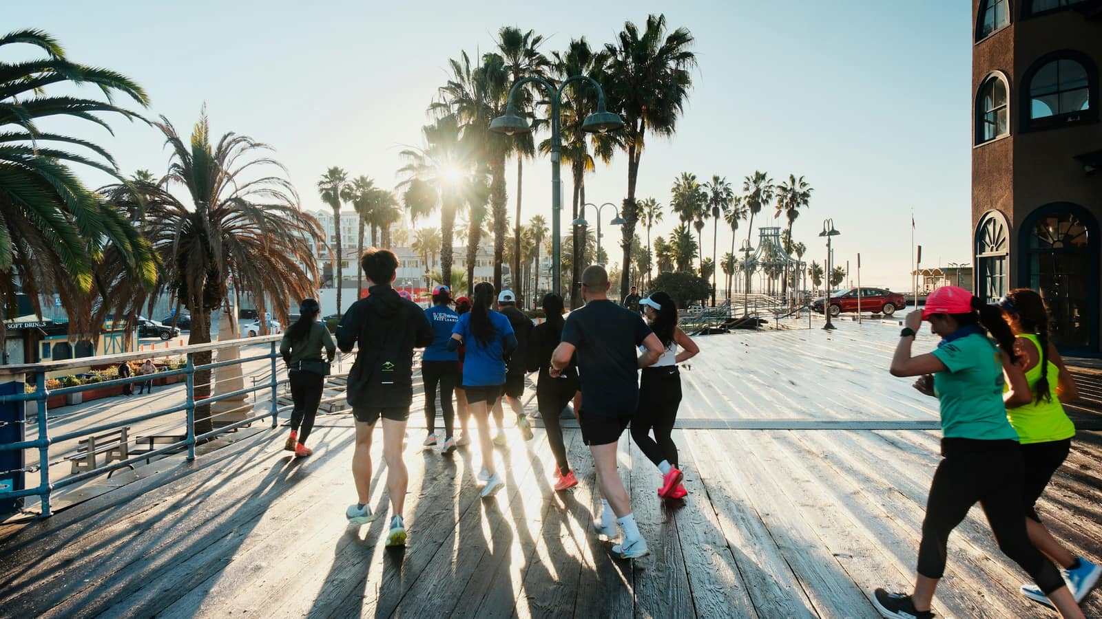 Run club heading out along a palm-lined waterfront boardwalk at sunrise — the easy group miles where IT band pain tends to show up, and the running that IT band syndrome physical therapy in Tampa gets you back to.
