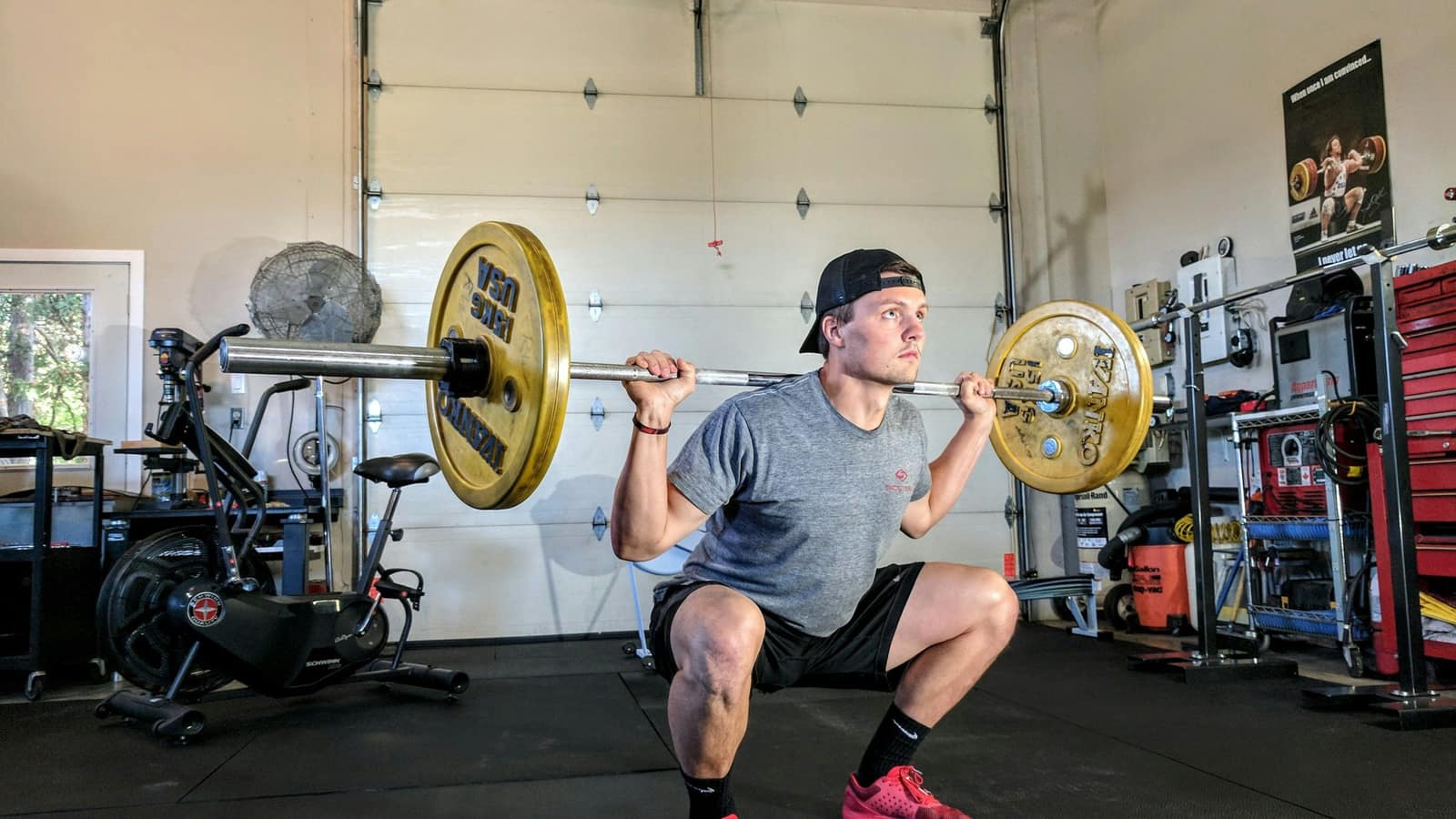 Lifter at the bottom of a deep barbell back squat in a home gym, knees fully bent under load — the deep squat that meniscus tear physical therapy in Tampa gets athletes back to.