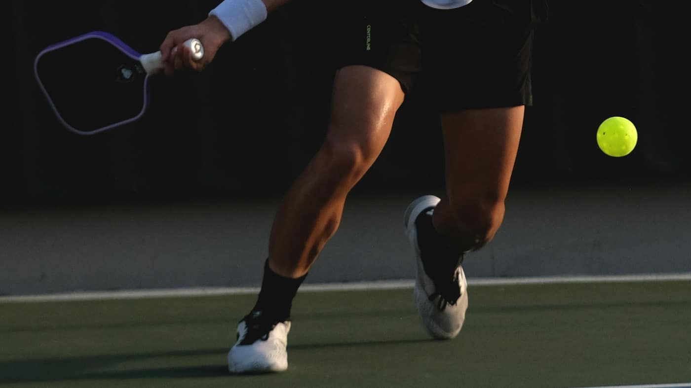 Pickleball player lunging on a planted foot with both knees bent to reach a low ball — the plant-and-twist behind many meniscus tears in Tampa Bay court athletes.