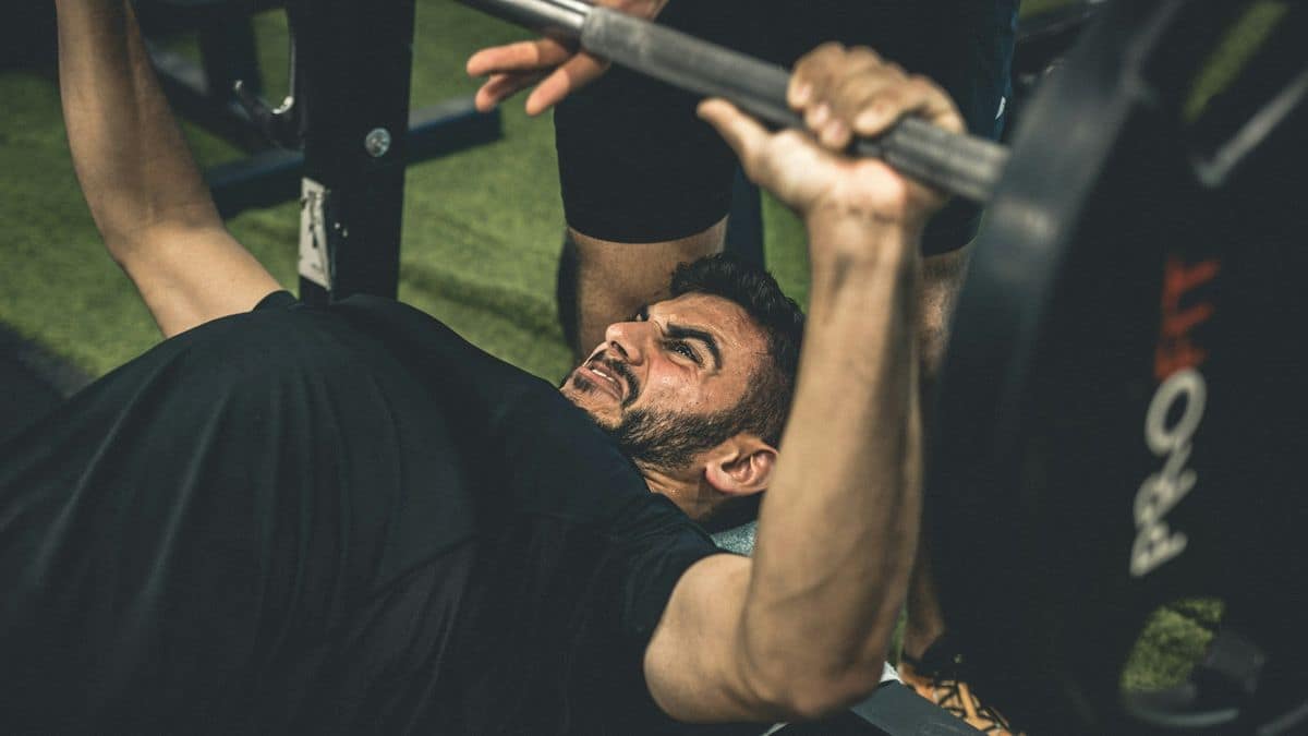 Lifter pressing a heavy barbell on the bench with a spotter &mdash; shoulder pain physical therapy for Tampa lifters at Forward Physio
