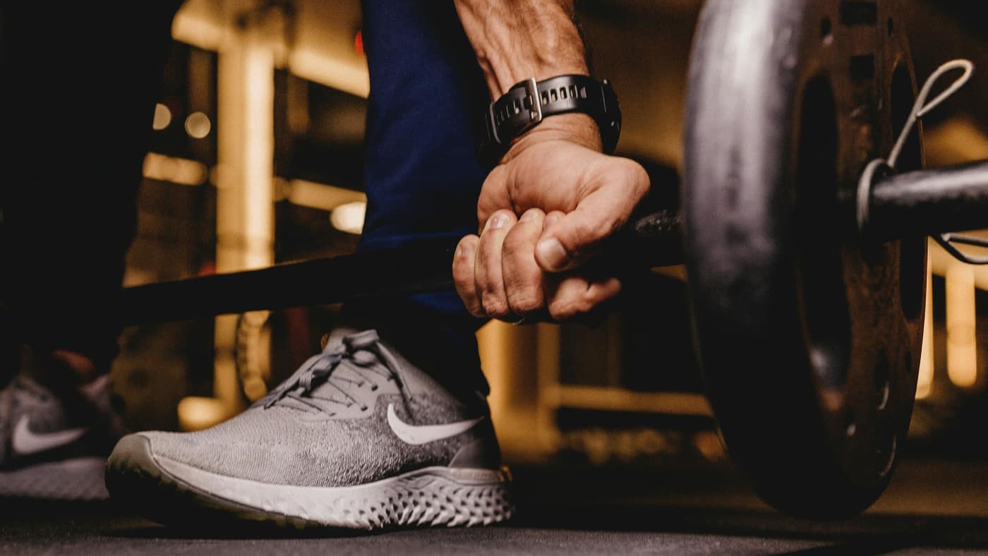 Lifter’s hand gripping a loaded barbell before a deadlift — the heavy grip work that tennis elbow rehab for Tampa lifters manages rather than stops.